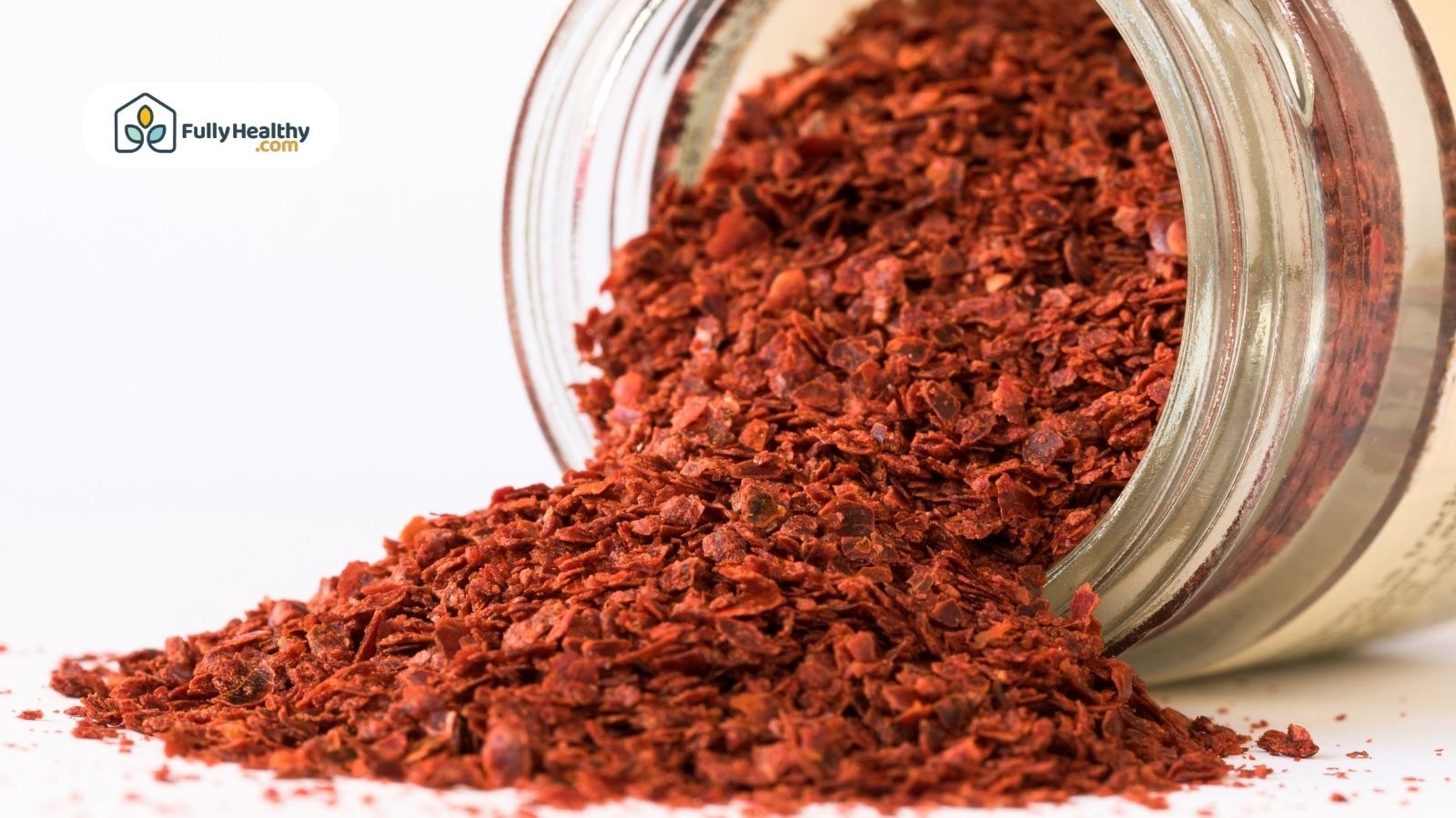 Glass jar of Aleppo pepper flakes spilling onto white surface