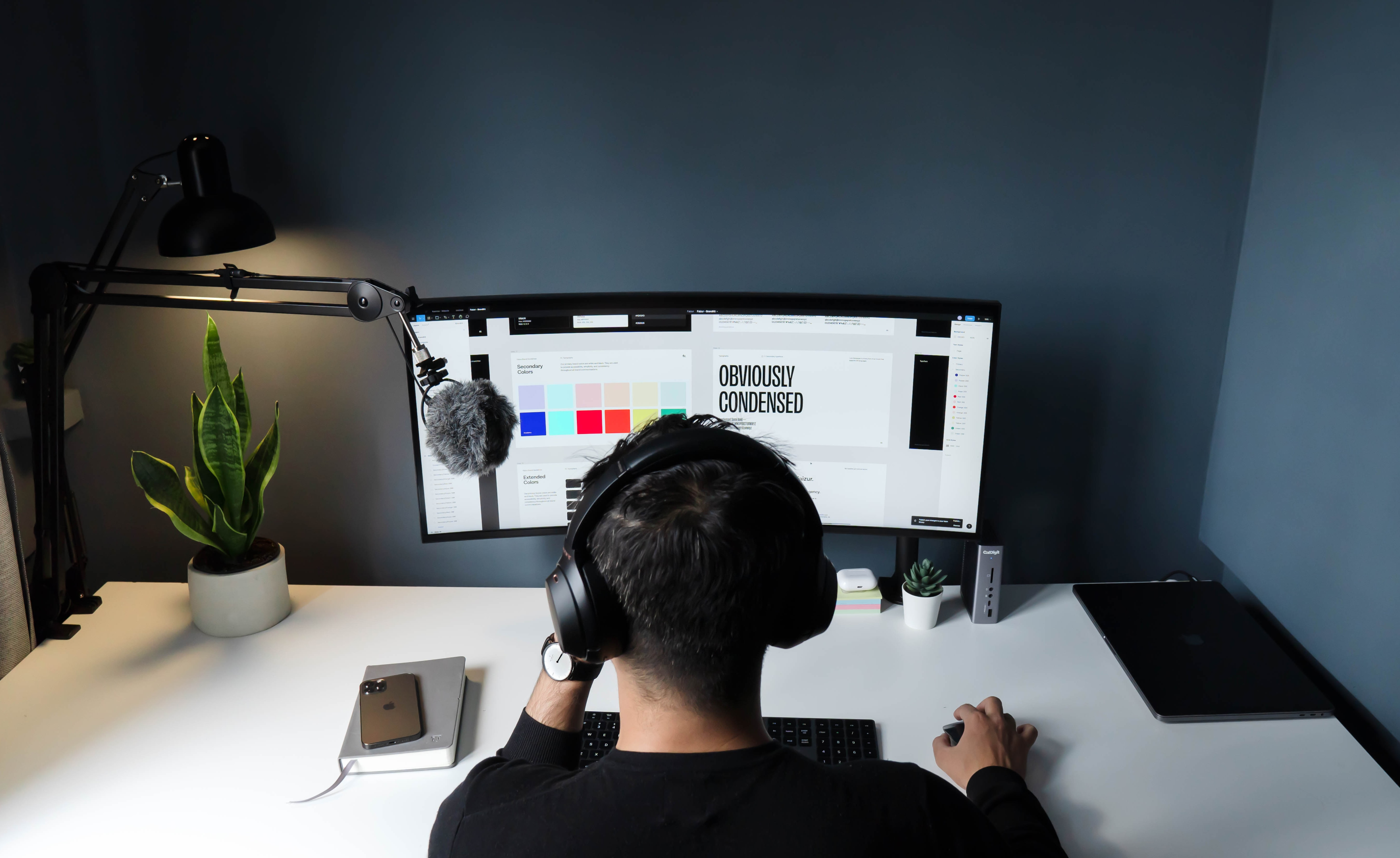 Un infographiste assis devant un grand écran, portant un casque de musique sur la tête. Il travaille sur la vectorisation de logo.