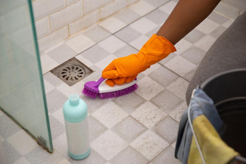 Person scrubbing shower floor grout with a brush and cleaning solution