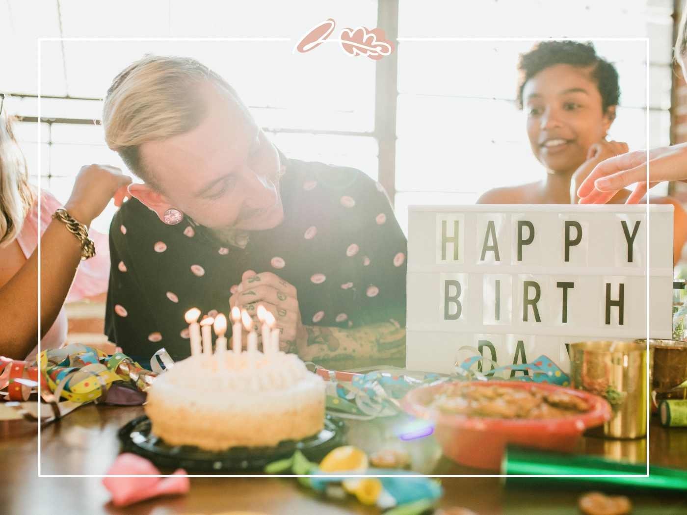 Birthday Wish for Boyfriend – birthday boy looking down at cake while friends cheer near a “Happy Birthday” sign and snacks