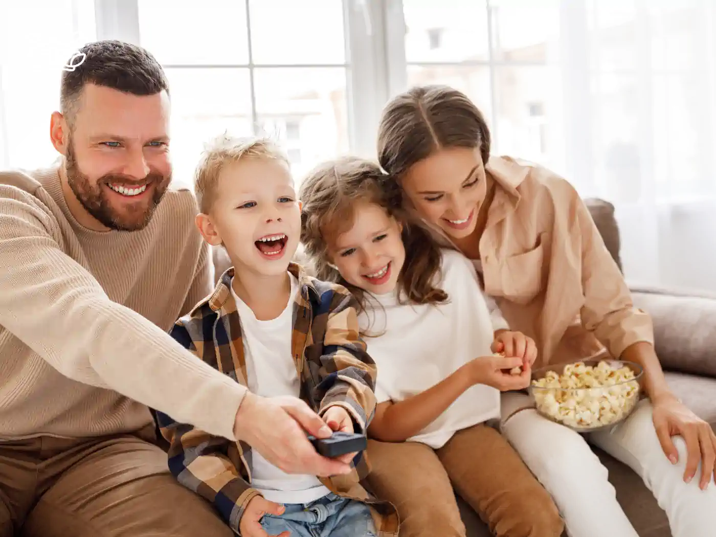 A joyful family sitting on a couch, watching TV, and enjoying a bowl of popcorn. Fabulous Flowers and Gifts, Snack and Fruit Hampers Collection.