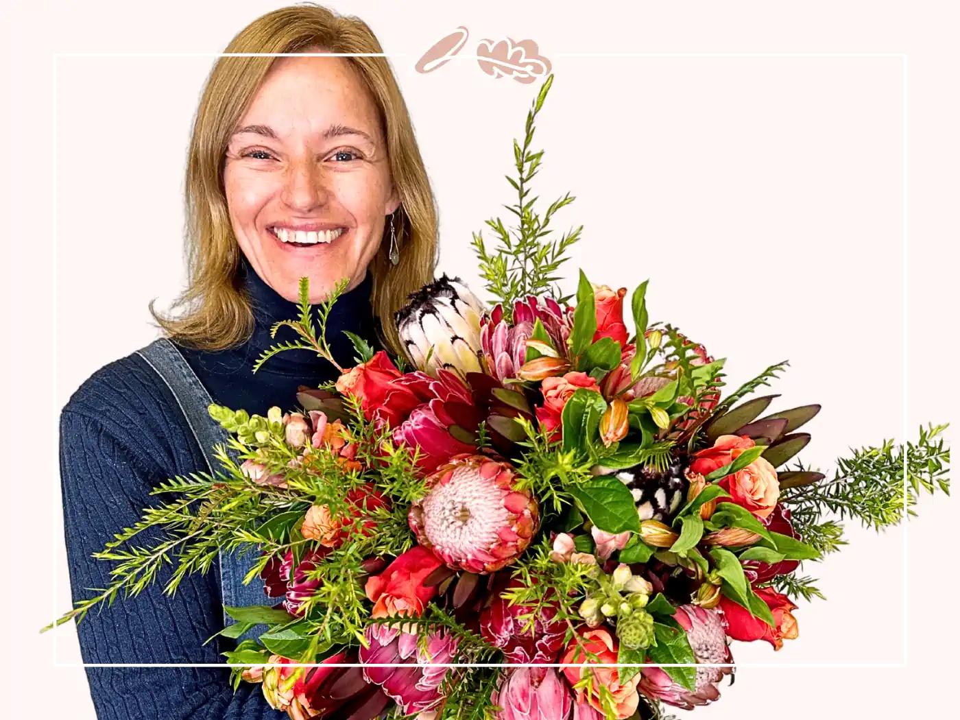 A smiling woman holding a vibrant bouquet of assorted flowers, including roses and proteas, against a white background. Fabulous Flowers and Gifts.