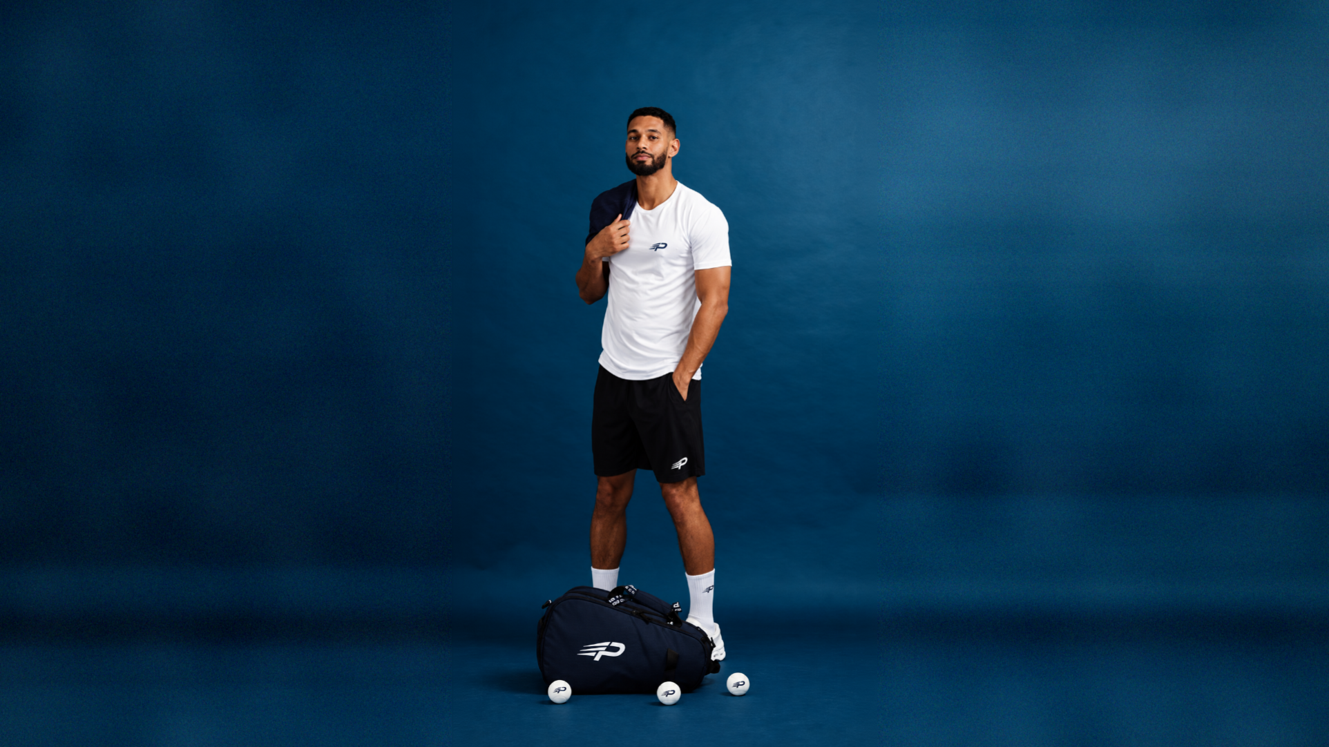A man is playing padel on an enclosed glass court, lunging for a low volley while wearing lightweight athletic clothing designed for maximum performance. His outfit features breathable fabrics and moisture-wicking technology, ideal for the dynamic movements and intense rallies of the padel game.