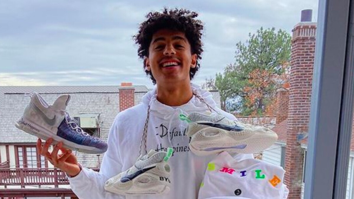 Smiling college basketball player holding multiple pairs of branded sneakers and a hoodie labeled 'SMILE,' promoting his NIL endorsement with an athletic footwear brand.