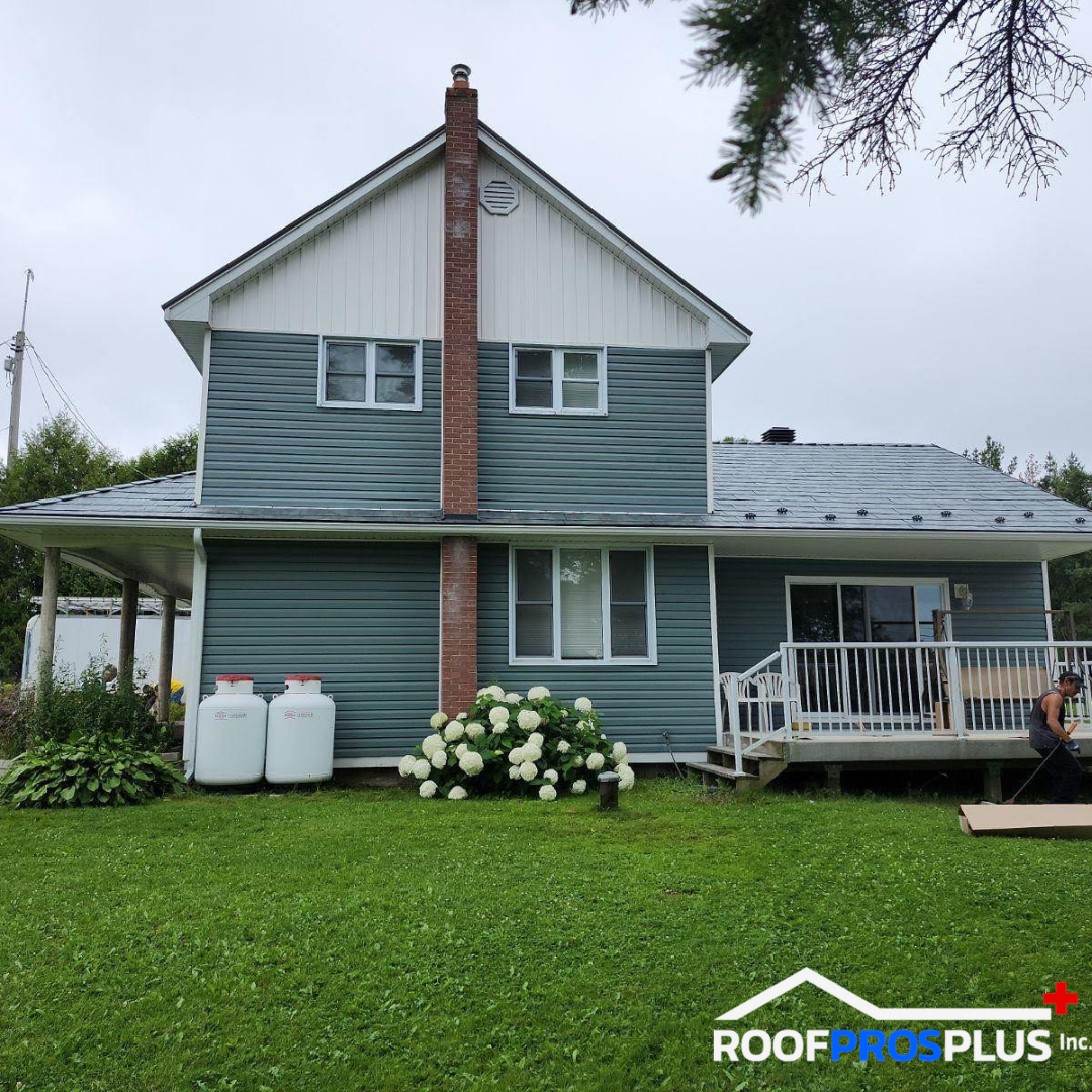 A house featuring blue siding and a metal roof, set against a clear sky and a beautiful lawn.