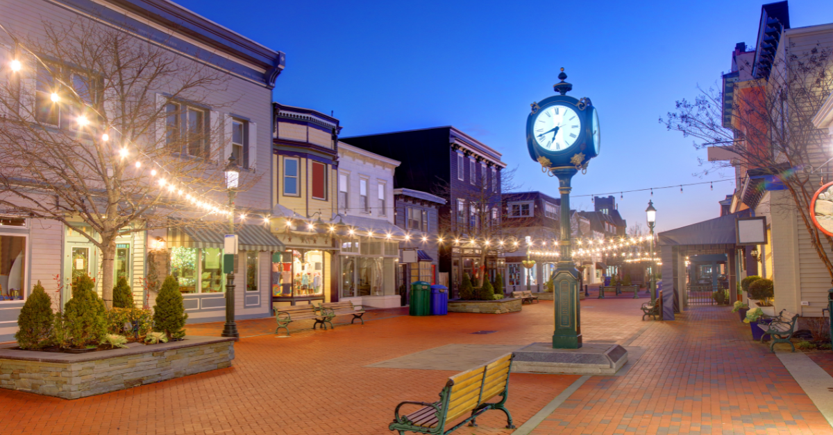 Evening view of Washington Street Mall with glowing string lights, historic storefronts, and a decorative clock in Cape May, NJ.