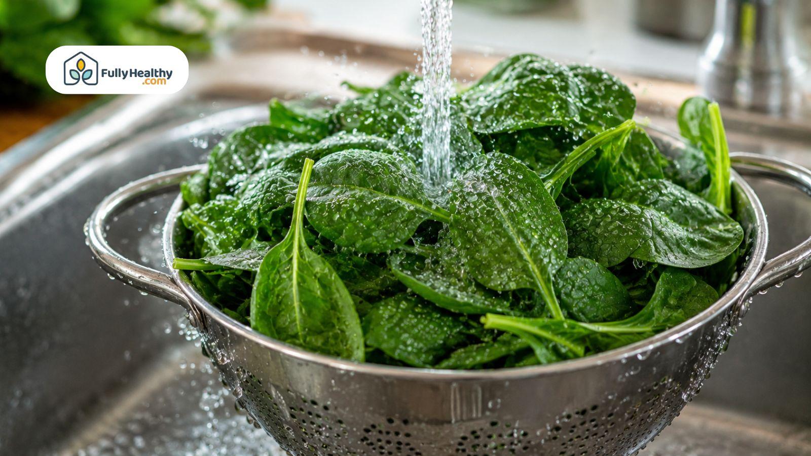 Fresh spinach leaves being rinsed under running water in a kitchen sink.