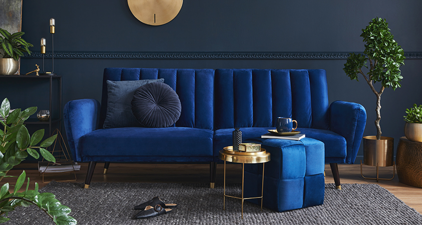 This living room uses houseplants to break up the dark blue colour palette, while the velvet sofa and ottoman give the room a cosy touch and shine under natural light.