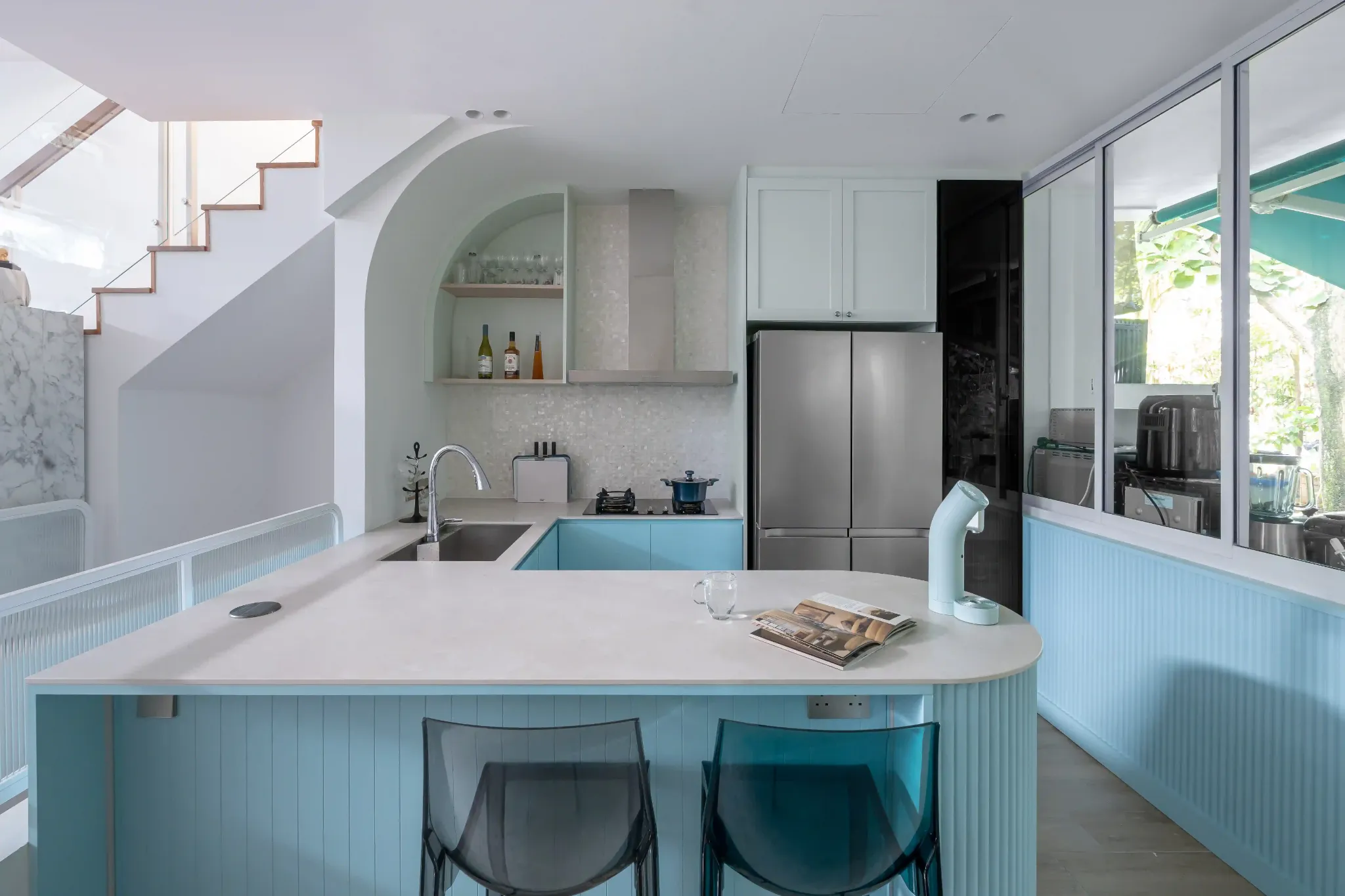 U-shaped kitchen with soft blue cabinets, arched niche and glass panels that keep the 4-room HDB living area connected.