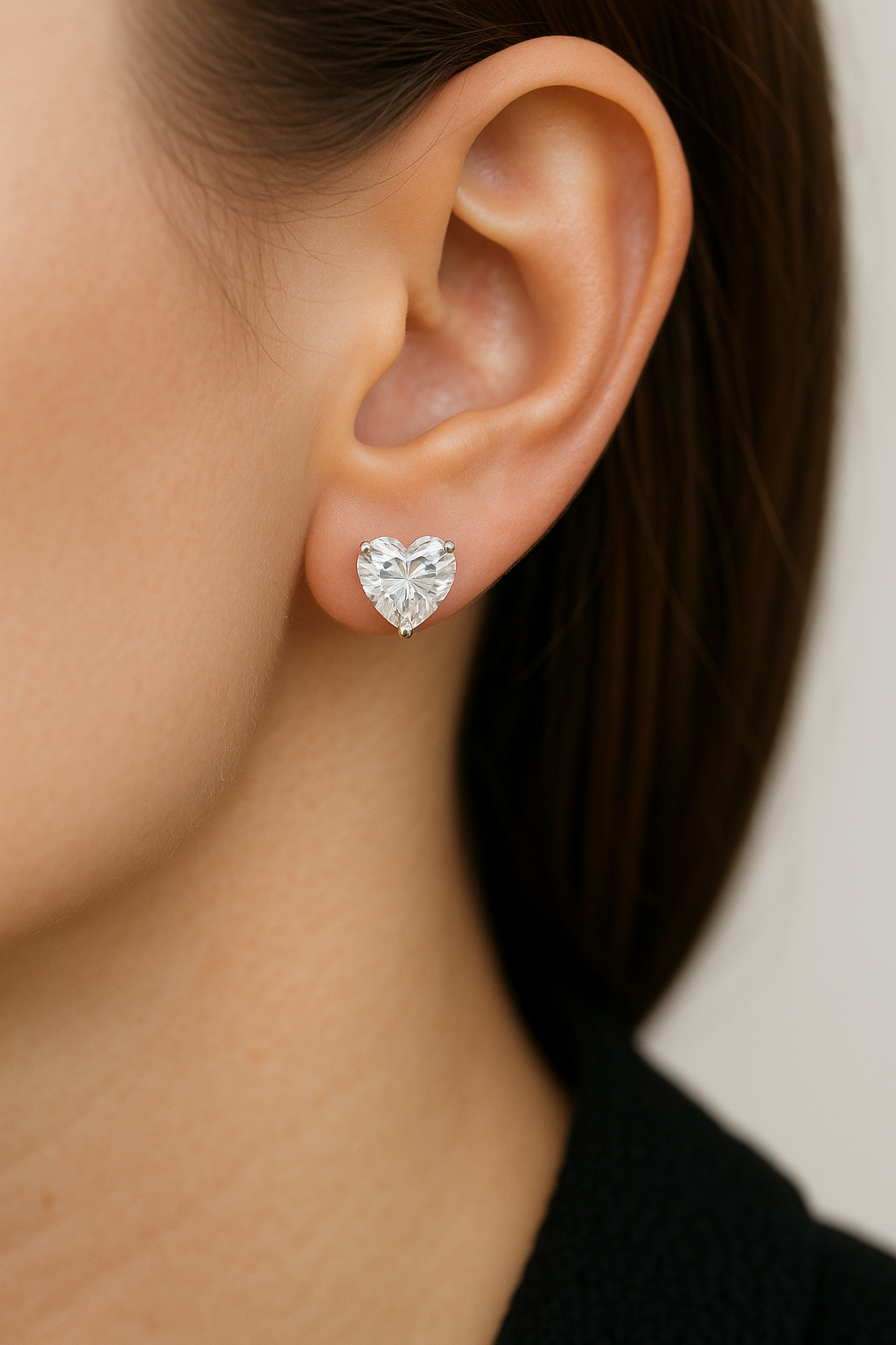 Baltos aukso auskarai su širdelės formos deimantais ant stilingos merginos ausies.