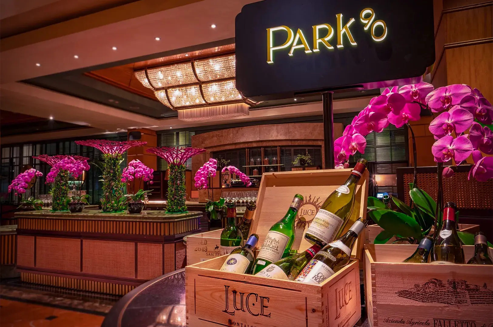 Elegant wine bar interior with a "Park90" sign above. Vibrant pink orchids and wine bottles in wooden crates create a luxurious and inviting atmosphere.