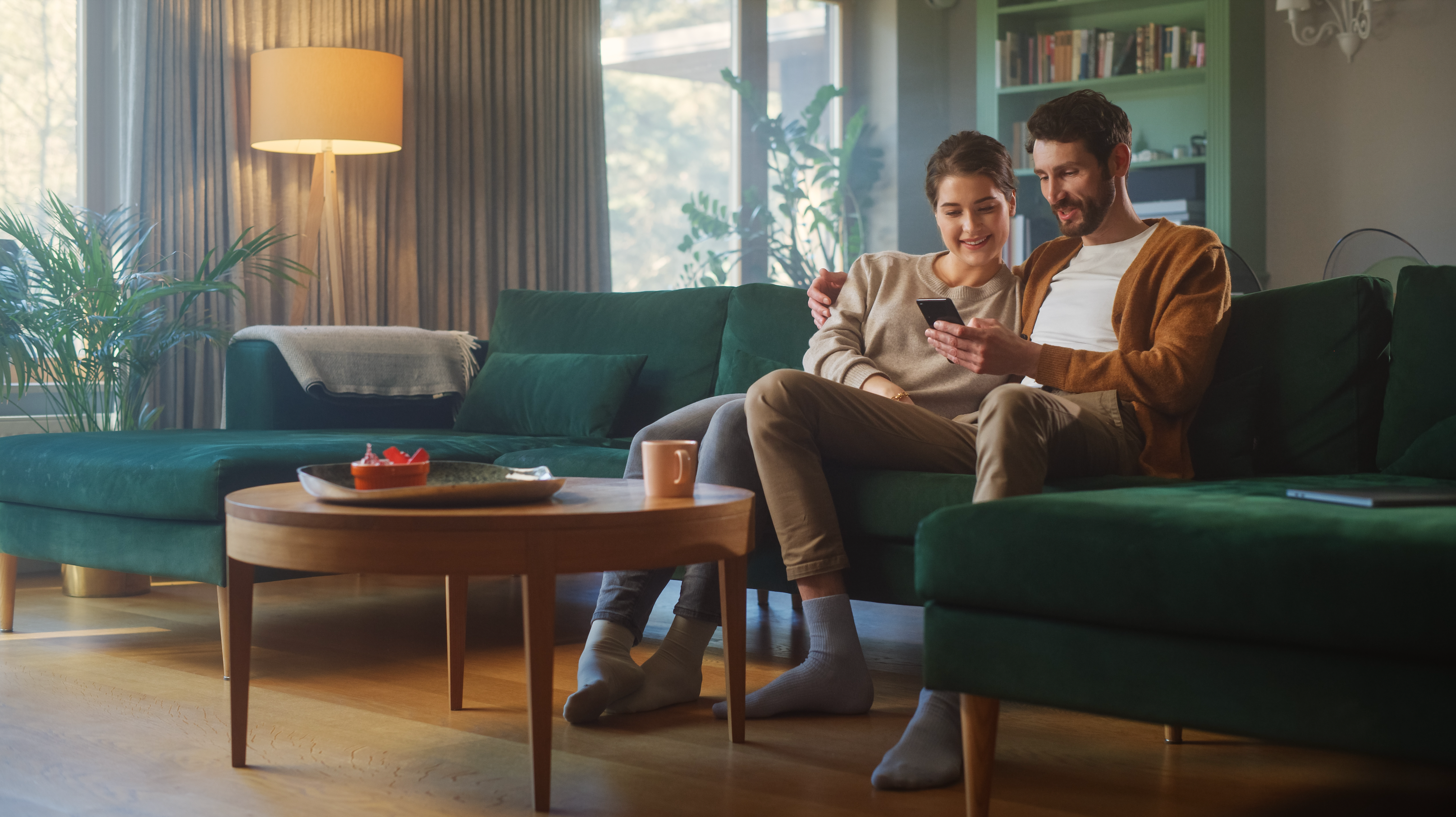 a man and woman sit next to each other on the couch and watch a mobile device he is holding