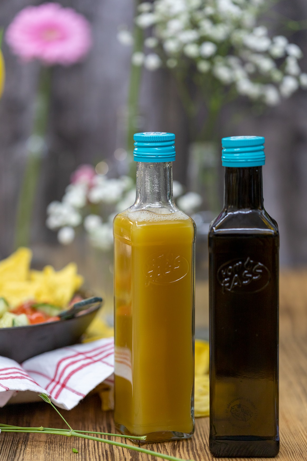 In the image, various colorful vinegars are displayed in glass bottles, showcasing different types such as balsamic vinegar, apple cider vinegar, and red wine vinegar. Each bottle highlights the unique colors and textures of the vinegars, emphasizing their potential use in salad dressings and marinades.