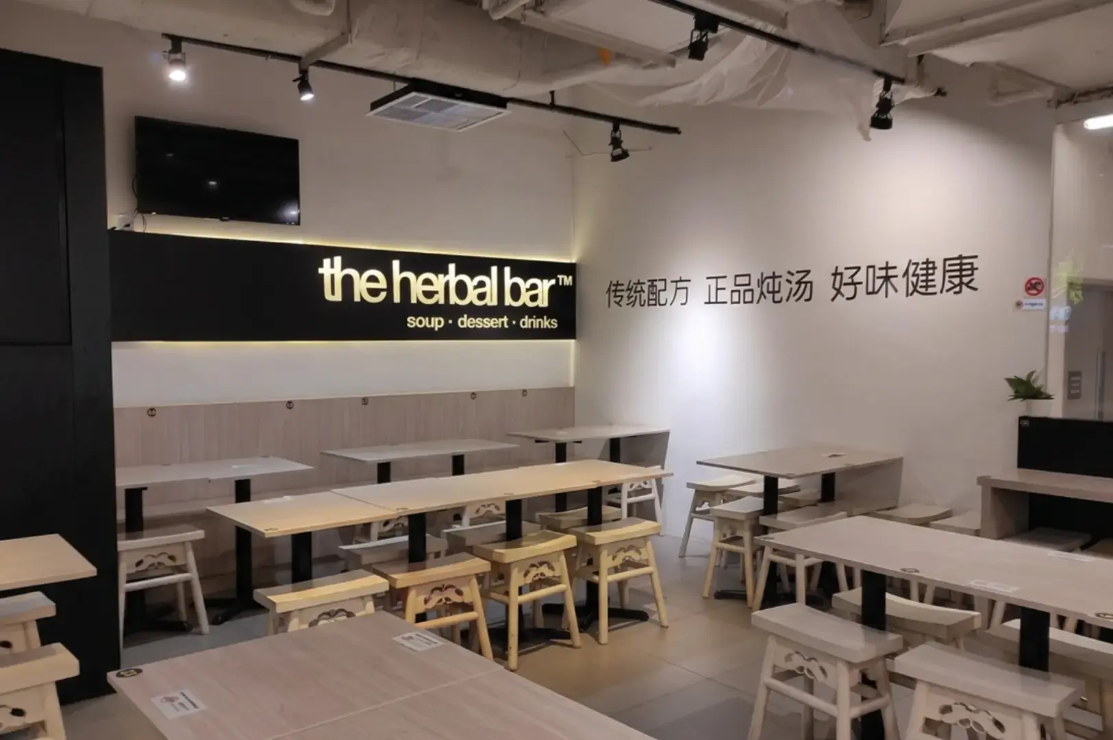 The Herbal Bar minimalist interior with light wood tables, benches, black wall signage, and Chinese text.