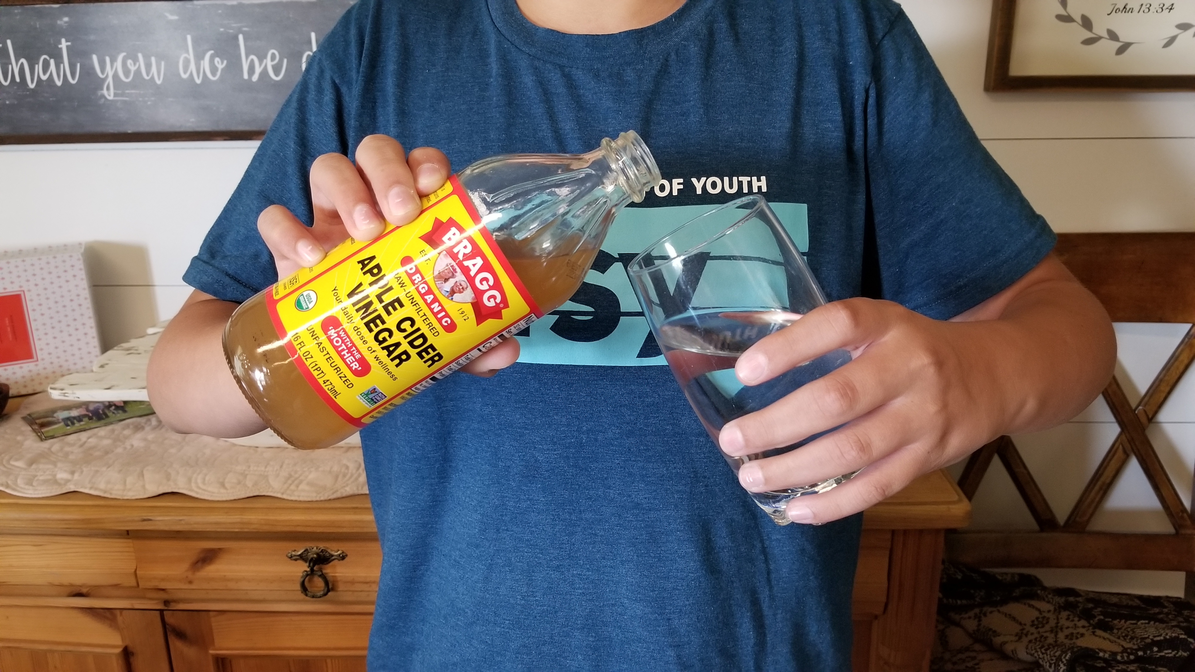 A person holding a bottle of apple cider vinegar and a glass of water