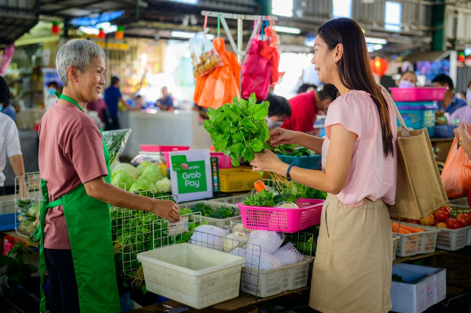 A smiling vendor and customer at a vibrant market stand, exchanging fresh green vegetables. The scene is lively, with colorful produce and a friendly tone.