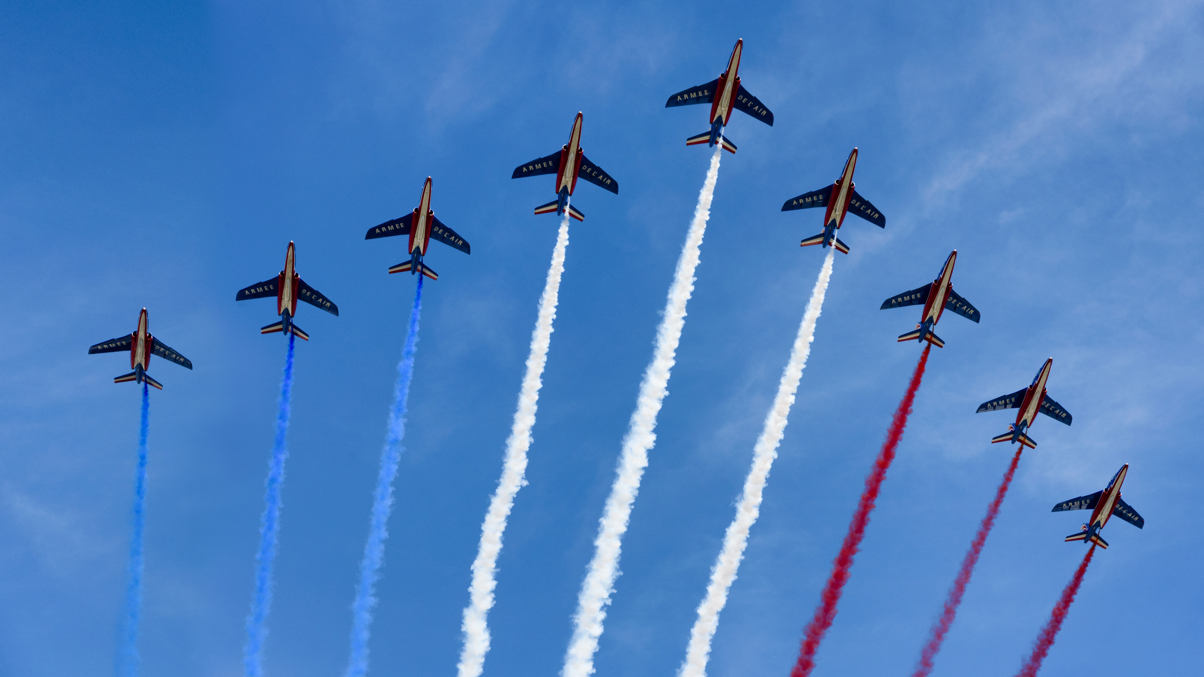 Nine stunt jets flying overhead with blue, white and red smoke.