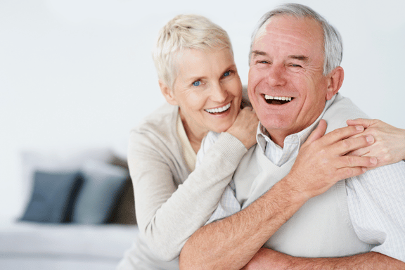 happy senior couple smiling with their arms wrapped over each others shoulders