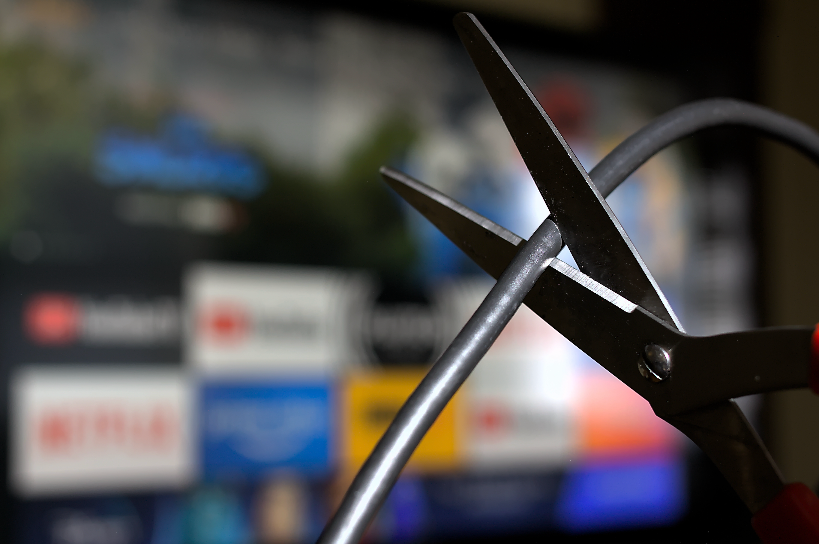 a pair of scissors is about to cut a cable cord while streaming apps are blurred in the background