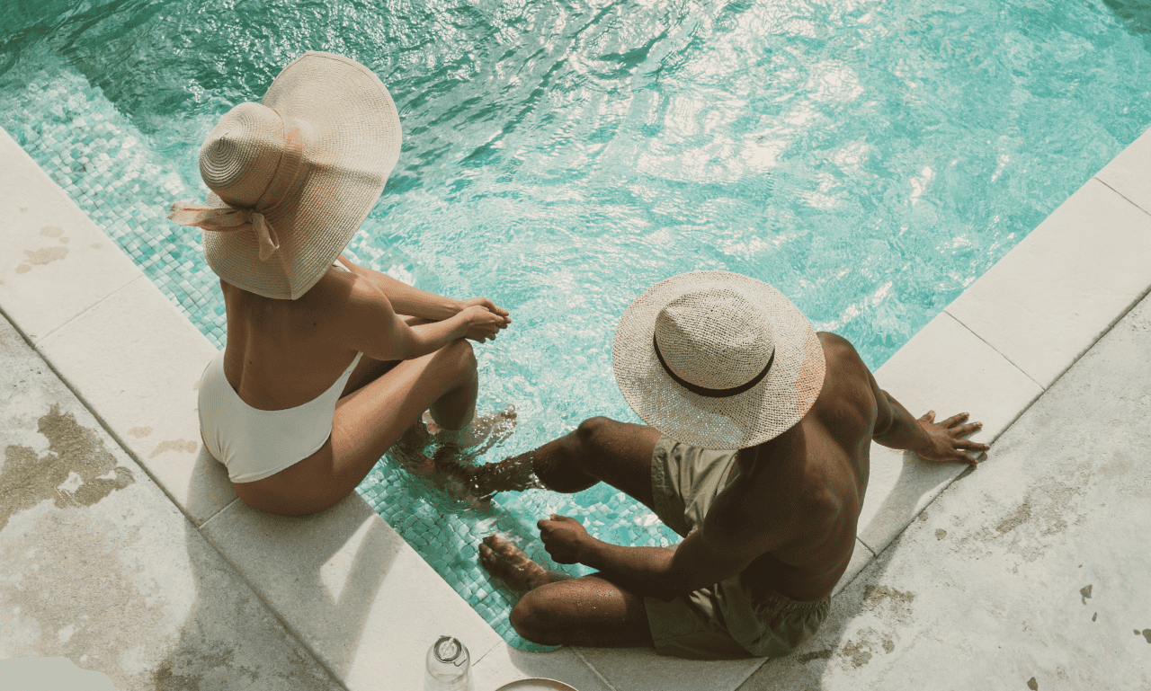 Couple sitting by the pool with hats on.