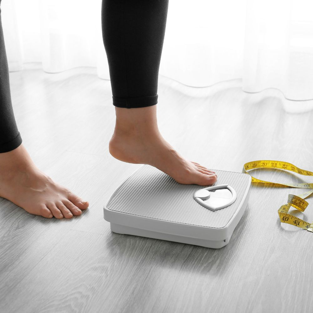 A person measuring their body weight reduction after successful weight loss journey with a scale