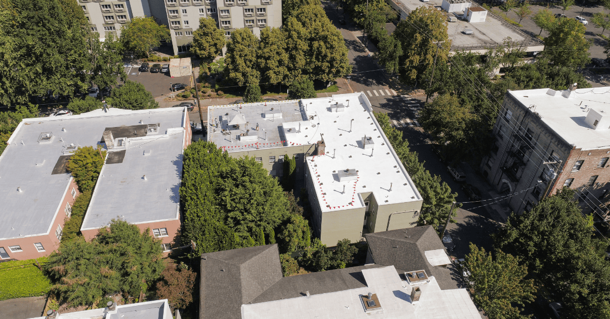 Drone image of commercial flat roofs with white reflective membranes in an urban setting.
