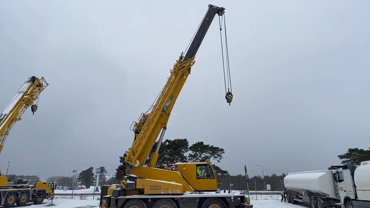 Yellow mobile cranes operating in a snowy construction site with cloudy skies, emphasizing industrial equipment during winter conditions