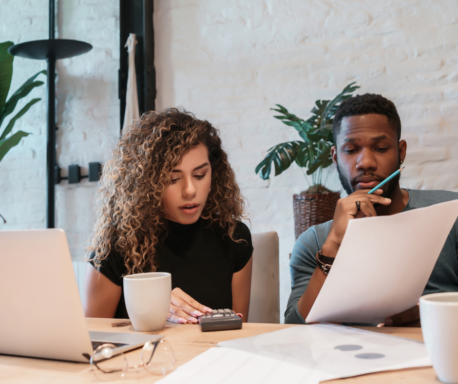 a man and woman calculate values while looking at paper and a laptop