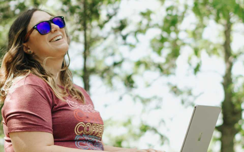 content writer and co-Founder of Trebletree, Megan laughs while working on her laptop ouside