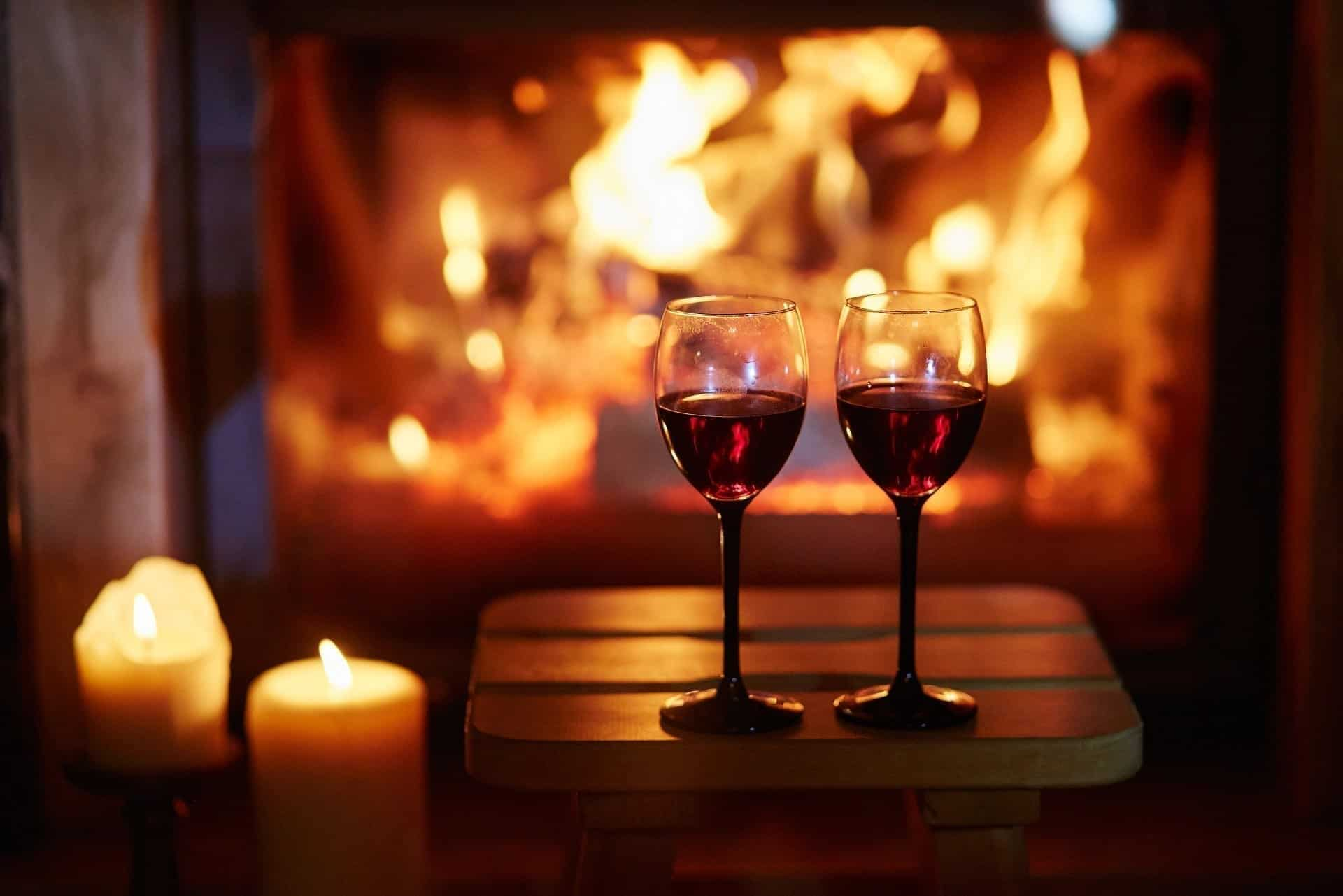 two glasses of red wine a table in front of a fire