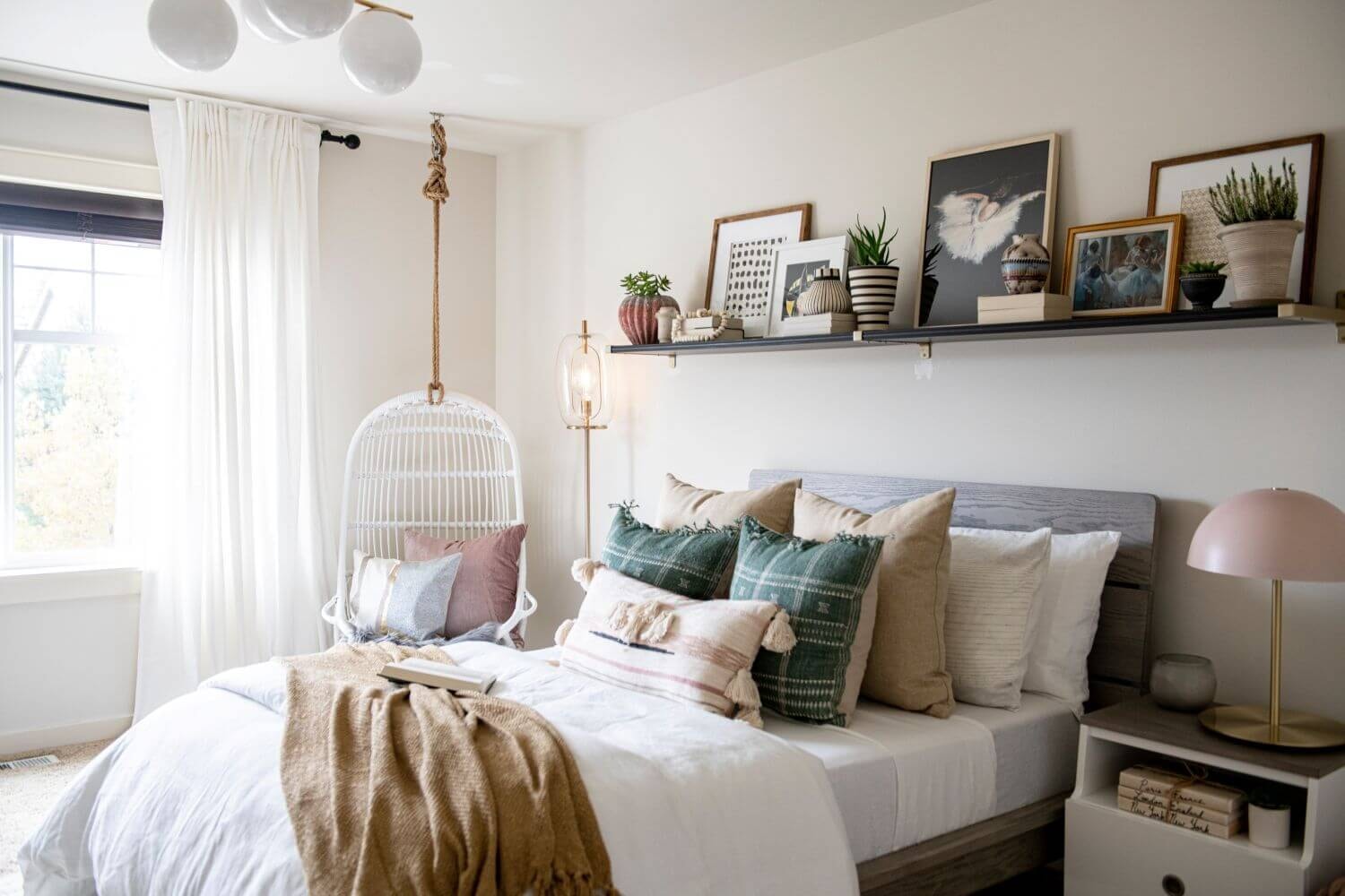 A cosy teenage girl's bedroom features a hanging chair with various pillows on the bed. The decor includes wall-mounted shelves and colorful wall art, creating a stylish and functional environment for a teen girl.