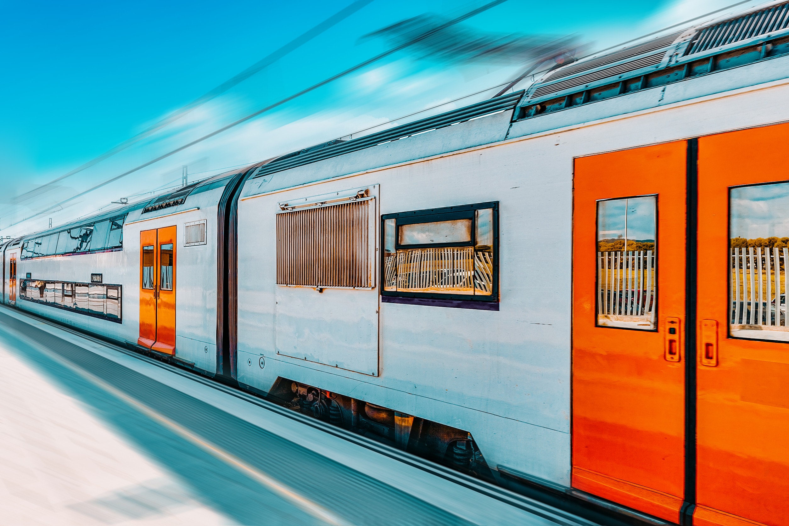 A silver train with orange doors stopped at a train station