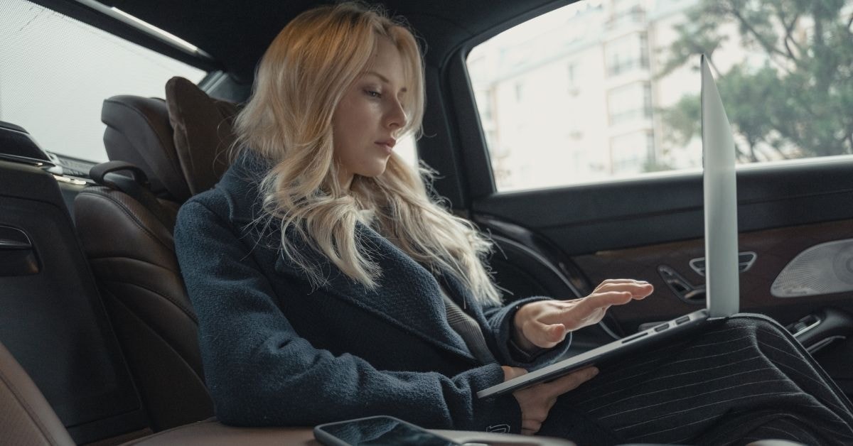 Woman in a luxury car using her laptop for luxury tax planning and financial management.