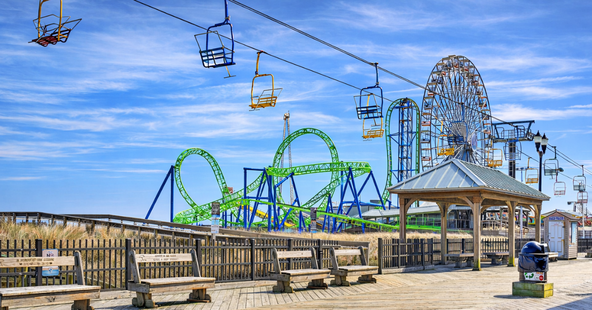 The iconic Seaside Heights boardwalk featuring a sky ride, Ferris wheel, and thrilling roller coasters under a bright blue sky — just minutes from your vacation rental.