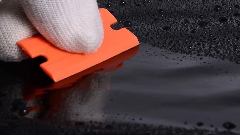 An orange plastic razor blade on a black car