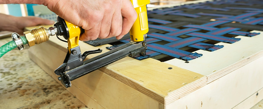 A close up of someone installing webbing support on a wooden frame.