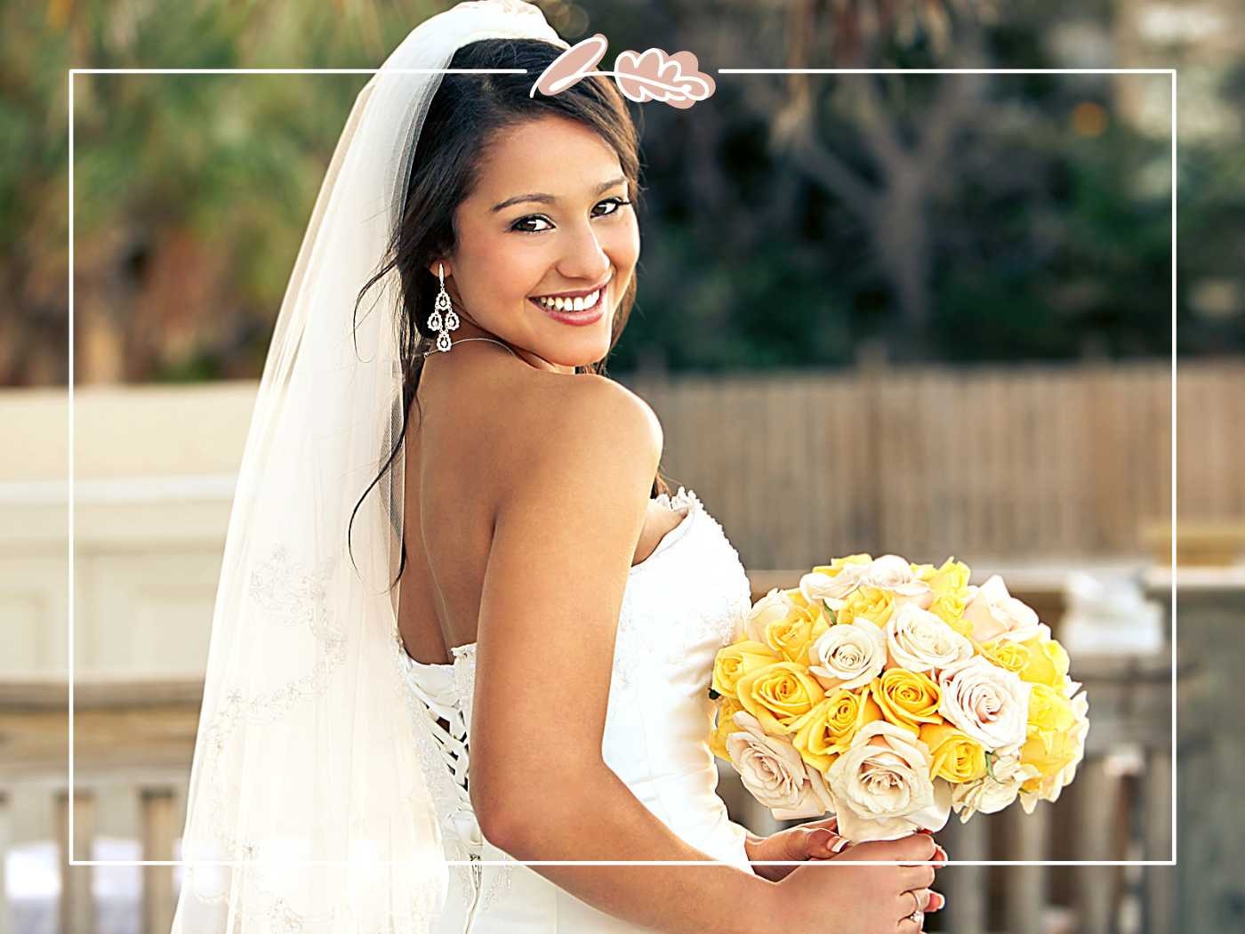 A smiling bride posing with a lovely bouquet of yellow and white roses, looking stunning on her special day. Fabulous Flowers and Gifts.