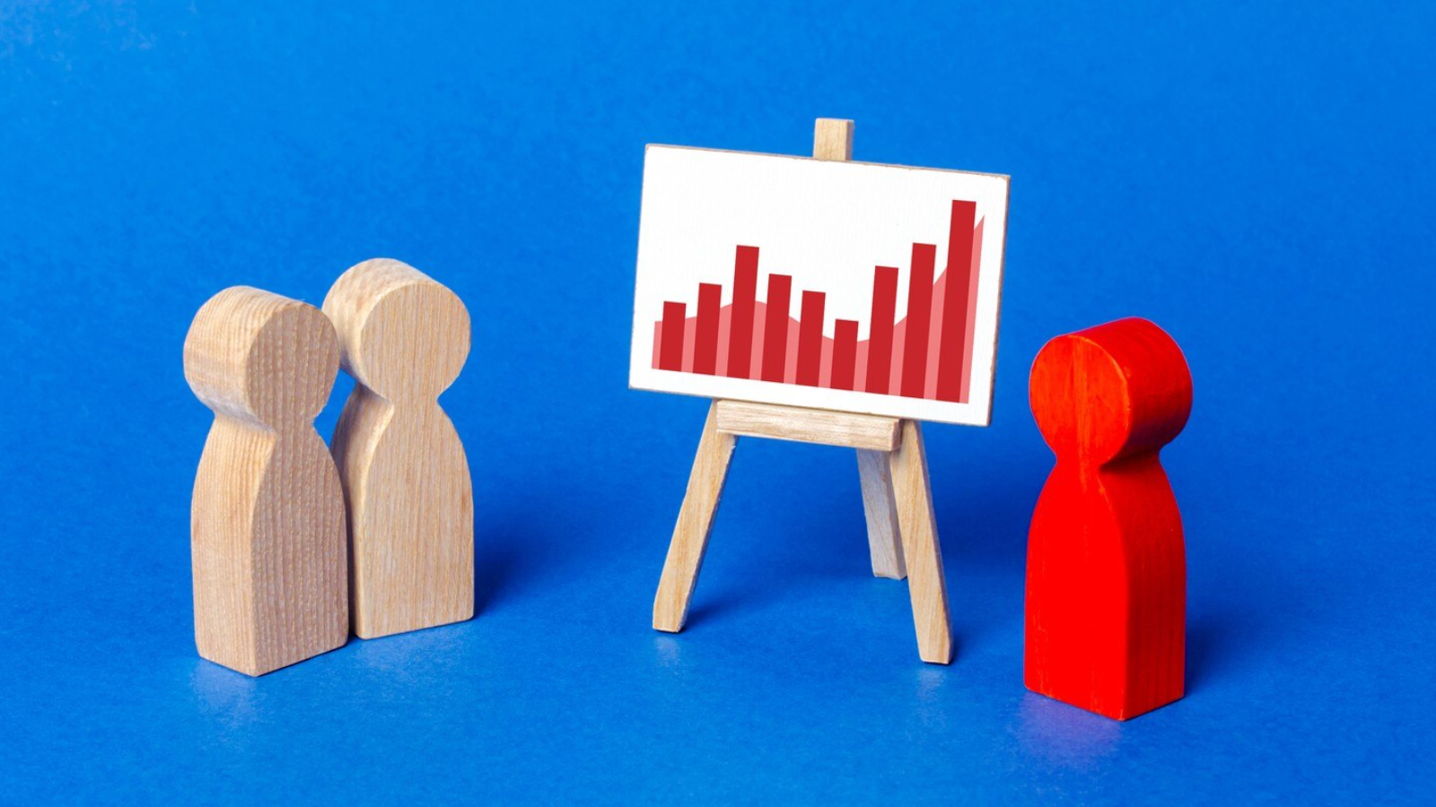 Red and neutral wooden figures reviewing a red bar chart, symbolizing a specialized marketing agency that uses targeted outbound marketing tactics.
