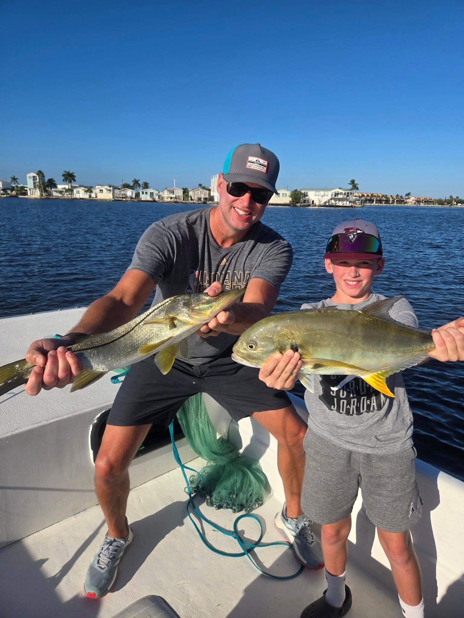a man and his son holding a snook and amberjack fish, hoping to catch trout near the shore of sanibel island, on their inshore fishing visit
