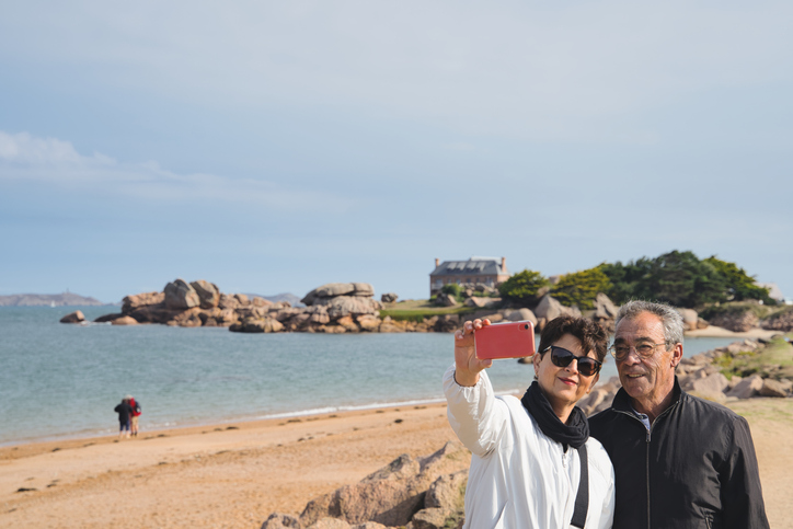 Cheerful mature couple bundled up on the beach and snapping a selfie. 