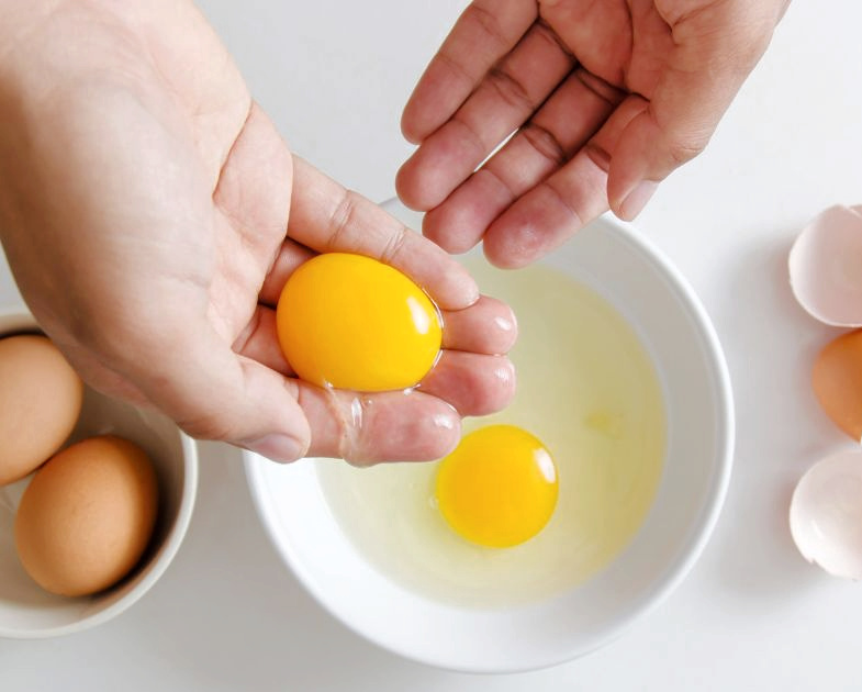 hands tossing yolk back and forth over bowl