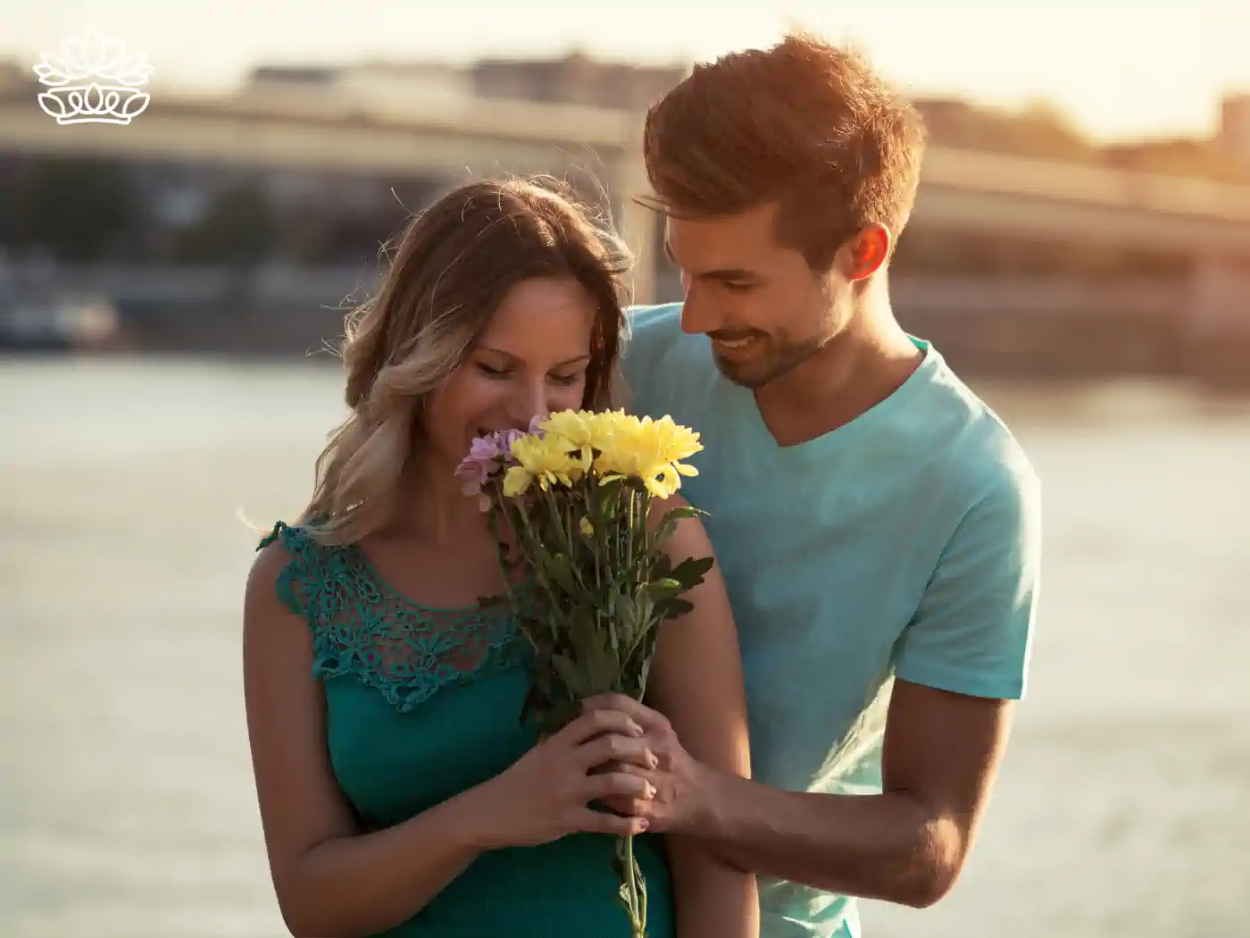 Image of a couple by the water, the man holding a flower bouquet while embracing the woman from behind. Fabulous Flowers and Gifts - Luxury Flower Bouquets.