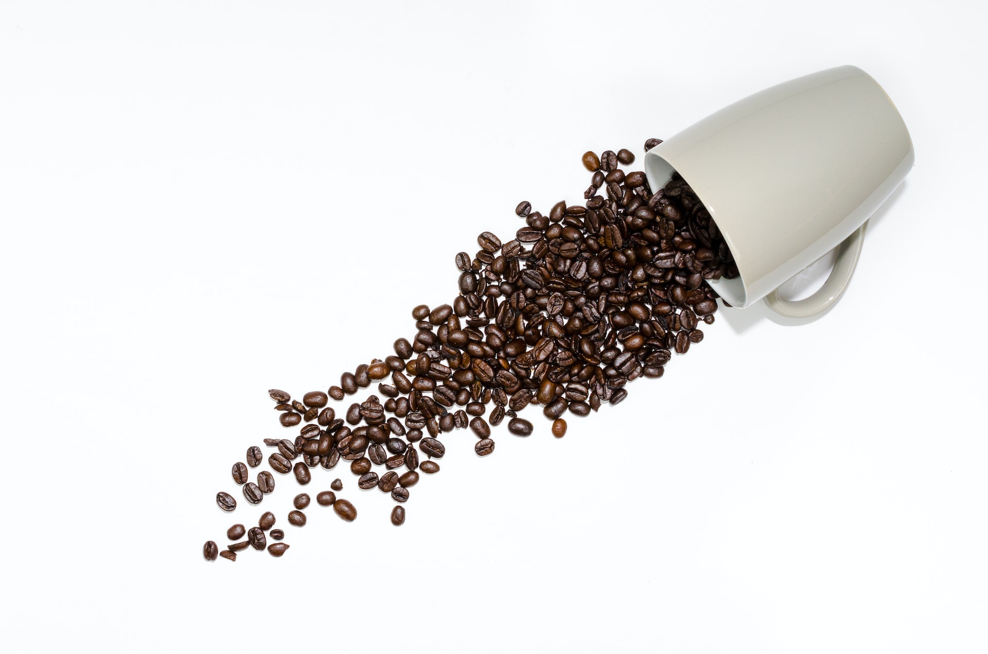 A knocked over white mug pouring out coffee beans