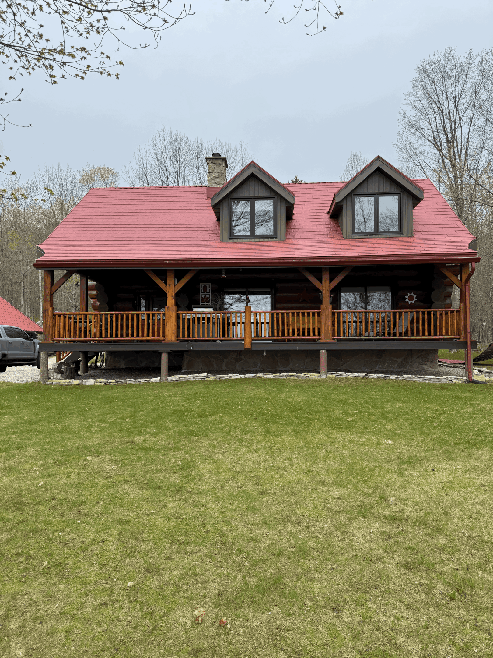 Charming log cabin with a bold red metal roof installation, surrounded by trees and open lawn.