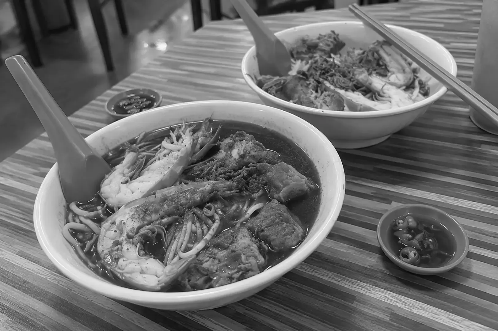 A hearty bowl of prawn mee filled with thick noodles, prawns, and savoury toppings in a deep-coloured broth.