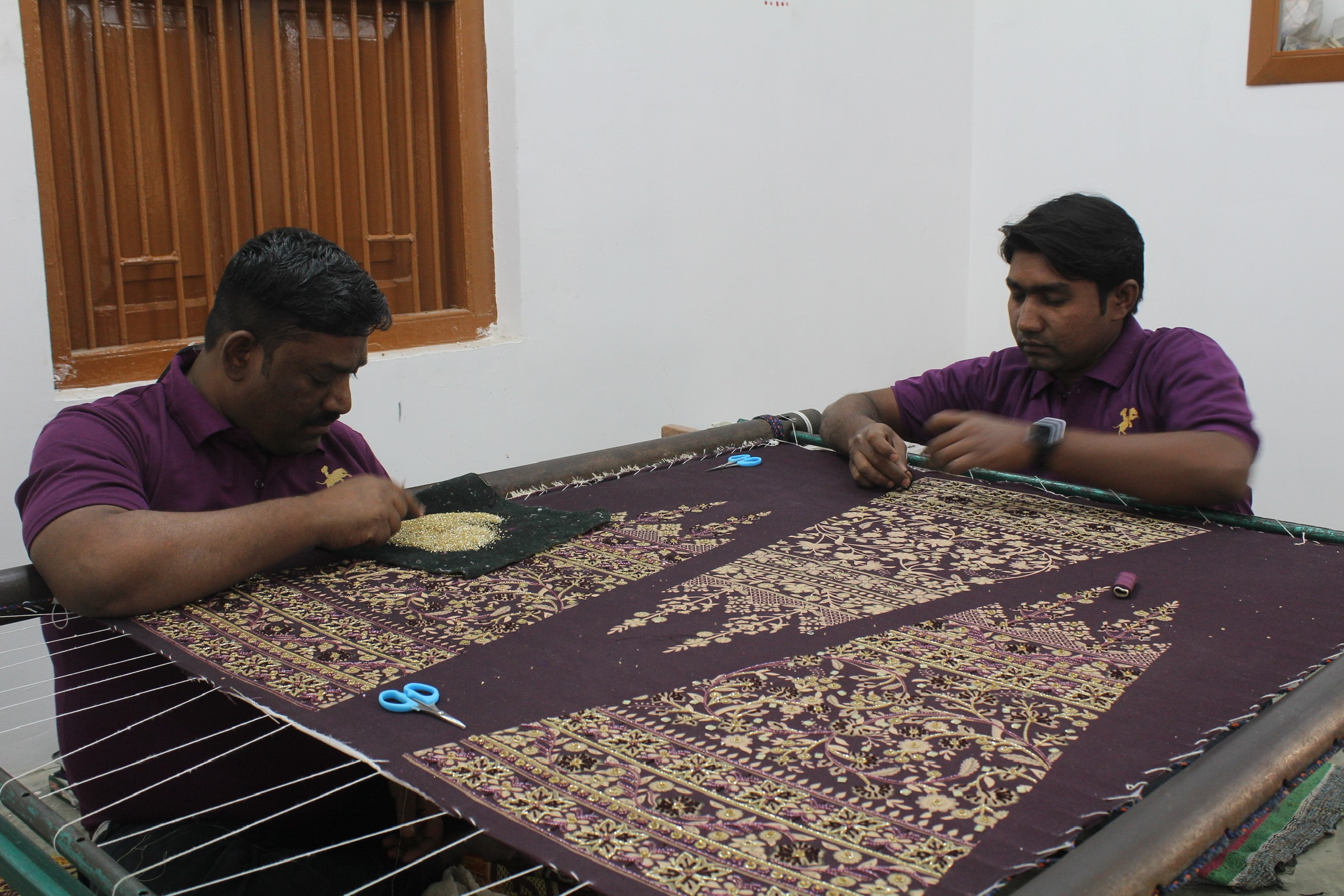 Skilled artisans is focused on creating intricate embroidery for a traditional lehenga, showcasing detailed patterns and vibrant hues. The craftsmanship highlights traditional motifs, adding elegance to this stunning piece typically worn during special occasions and weddings.