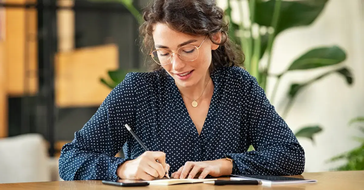 Female content creator writing income and expenses in notebook to understand what are liabilities.