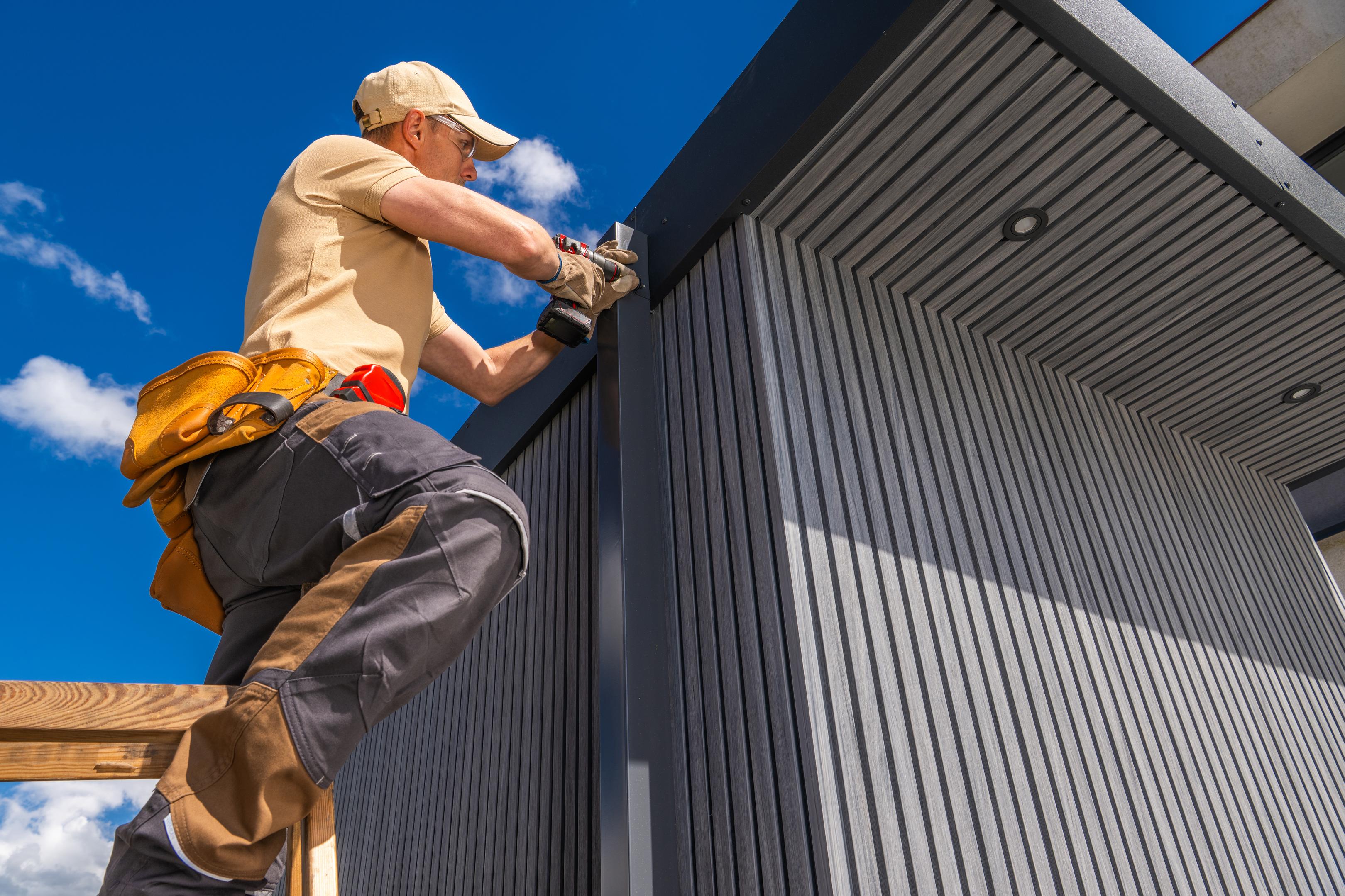 Worker on ladder installing panels on a building under clear blue sky