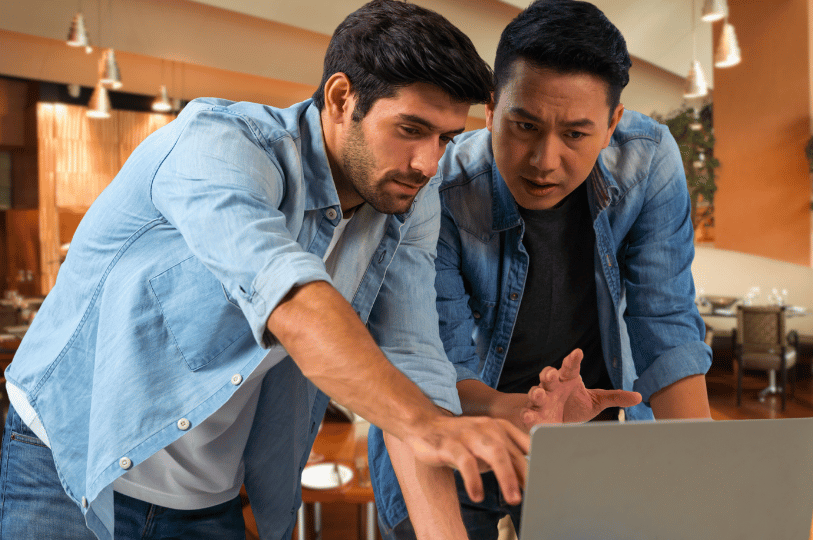 Two men leaning over a laptop with frustrated and confused expressions, pointing at the screen. This captures the common frustration of business owners trying to diagnose technical SEO issues or missing Google Business Profiles.
