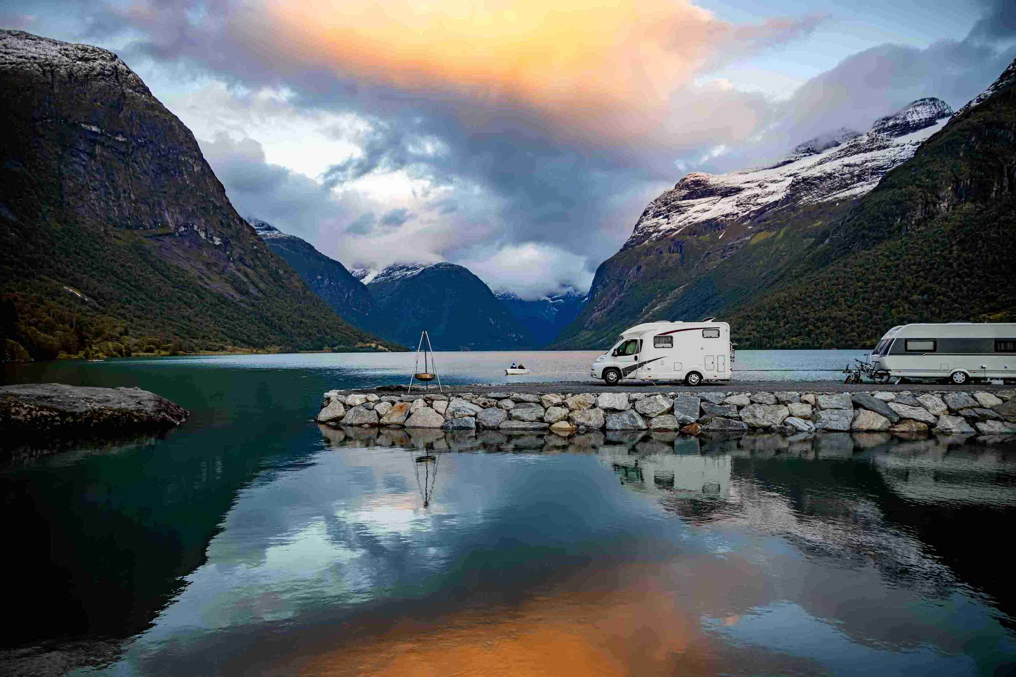 Caravaning w pięknej przyrodzie Norwegii. Dwa kampery zaparkowane jeden za drugim nad jeziorem otoczonym górami. 